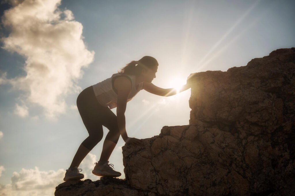 Vista de ángulo bajo de una mujer escalando formaciones rocosas contra el cielo durante un día soleado